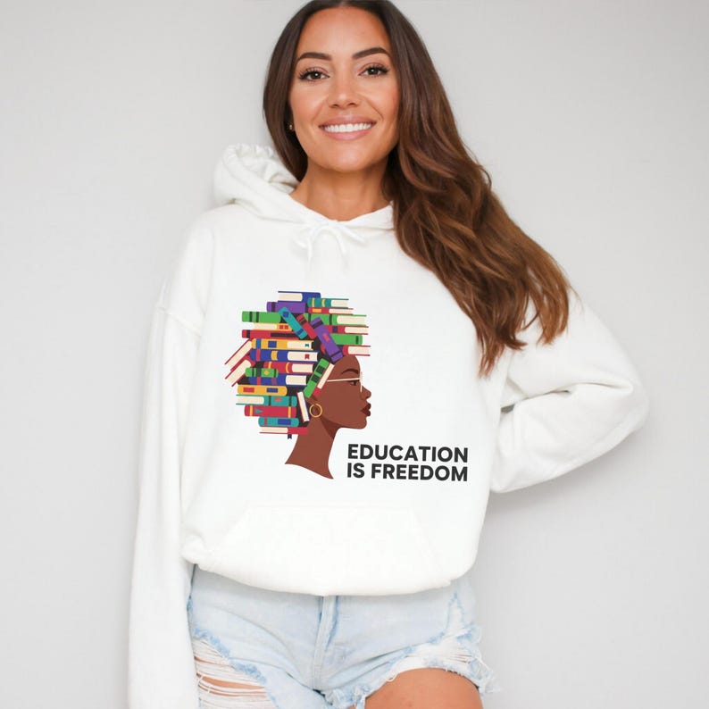 Puede incluir: Sudadera con capucha blanca con un gr&aacute;fico de un perfil humano con el pelo formado por una pila de libros coloridos. El texto "EDUCATION IS FREEDOM" est&aacute; impreso debajo. La sudadera tiene un bolsillo delantero y una capucha con cord&oacute;n.