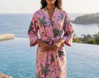 Puede incluir: Una bata rosa de manga larga con un estampado repetitivo de cebras, leopardos y palmeras. La prenda incluye un cinturón para anudar, dos bolsillos delanteros y un ribete blanco a lo largo de las solapas y la abertura frontal.