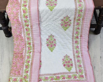 Puede incluir: Un edredón floral blanco y rosa con un borde a rayas. El edredón presenta un patrón floral repetido en rosa y verde sobre un fondo blanco. El borde es rosa con rayas blancas y un ribete rojo.