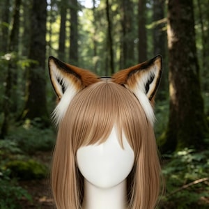 May include: A headband with fox ears. The ears are brown, white, and black, with a fluffy texture. The ears are attached to a black headband. The background is a blurred forest scene.