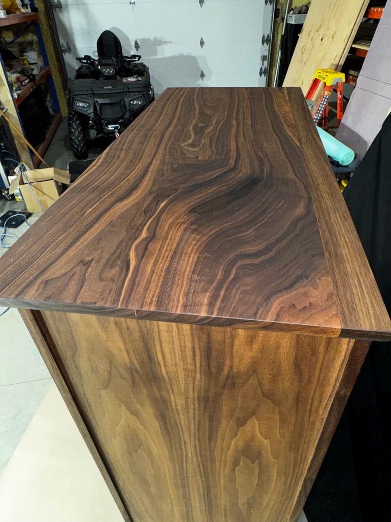 Puede incluir: Mesa de madera artesanal con acabado en nogal oscuro. La superficie superior muestra un patr&oacute;n de vetas de madera prominente, mientras que los lados tienen un tono de madera m&aacute;s claro y natural. El dise&ntilde;o es simple y moderno, mostrando la belleza natural de la madera.