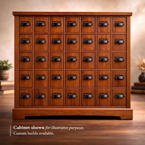 May include: A wooden cabinet with a warm brown finish, featuring a grid of small square drawers. Each drawer has a black handle. The cabinet has a rectangular shape and sits on a base. The text at the bottom says "Cabinet shown for illustrative purposes. Custom builds available."