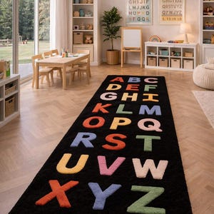 May include: A long, rectangular black area rug featuring the English alphabet in raised, multi-colored letters. Each letter is rendered in a soft, textured finish with a variety of colors including red, orange, yellow, green, blue, and pink.