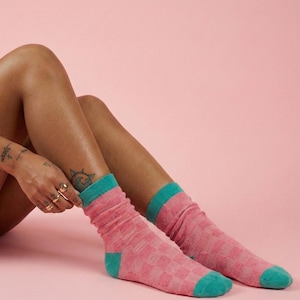 Könnte beinhalten: Rosa und türkisfarbene Socken mit Karomuster. Die Socken haben türkisfarbene Bündchen, Fersen und Zehen. Der Hintergrund ist einfarbig rosa.