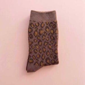 K&ouml;nnte beinhalten: Eine einzelne Socke mit einem braunen und goldenen Leopardenmuster. Die Socke hat eine ged&auml;mpfte braune Farbe mit einem dunkleren braunen B&uuml;ndchen und Zehen. Der Leopardenprint ist goldfarben.