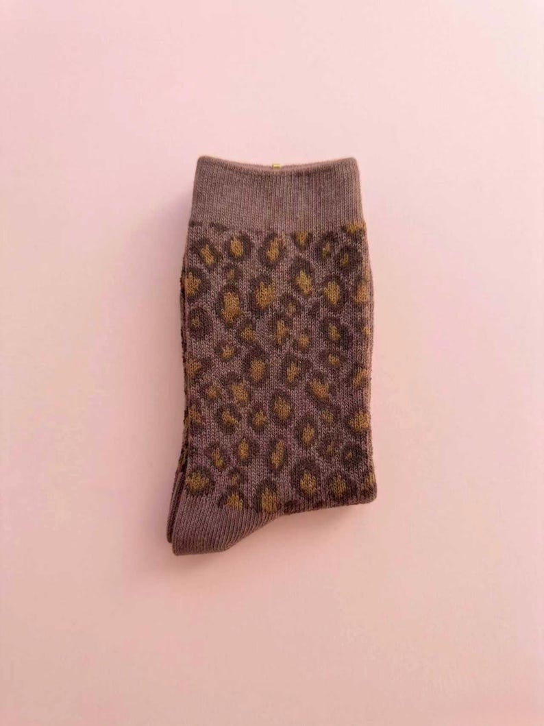 K&ouml;nnte beinhalten: Eine einzelne Socke mit einem braunen und goldenen Leopardenmuster. Die Socke hat eine ged&auml;mpfte braune Farbe mit einem dunkleren braunen B&uuml;ndchen und Zehen. Der Leopardenprint ist goldfarben.
