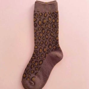 K&ouml;nnte beinhalten: Ein Set aus drei Keramikbechern mit cremefarbener, gesprenkelter Glasur. Jeder Becher hat ein handgemaltes Blumendesign in Blau-, Gr&uuml;n- und Gelbt&ouml;nen. Die Becher haben eine schlichte, moderne Form.