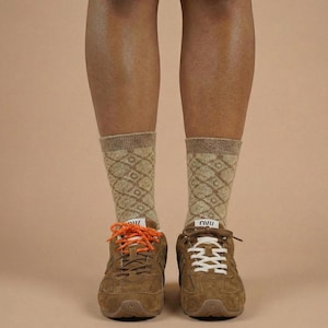 Könnte beinhalten: Braune Wildleder-Sneakers mit orangefarbenen und weißen Schnürsenkeln, kombiniert mit tanfarbenen Socken mit Rautenmuster. Die Sneakers haben ein klassisches Design mit einer gepolsterten Sohle und dem Buchstaben "N" an der Seite.