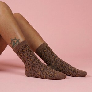 K&ouml;nnte beinhalten: Braune Socken mit Leopardenmuster. Die Socken reichen bis zur Mitte der Wade. Der Hintergrund ist einfarbig rosa.