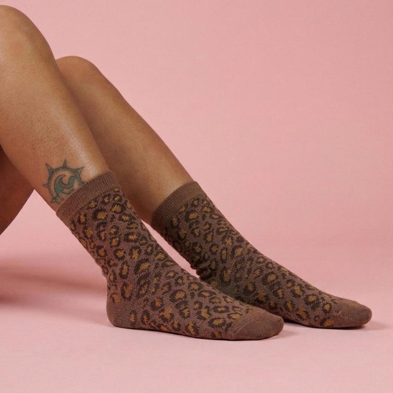 K&ouml;nnte beinhalten: Braune Socken mit Leopardenmuster. Die Socken reichen bis zur Mitte der Wade. Der Hintergrund ist einfarbig rosa.