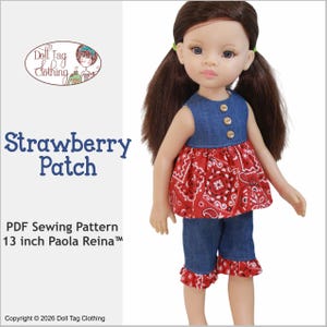 Peut inclure: Une poupée vêtue d'un haut en jean avec des boutons en bois, d'un haut péplum rouge à imprimé bandana et d'un short. Le short a des volants rouges à imprimé bandana. Le texte "Strawberry Patch" et "13 inch Paola Reina" sont visibles.