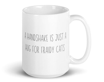 Puede incluir: Taza de café de cerámica blanca con texto negro que dice "A handshake is just a hug for fraidy cats".