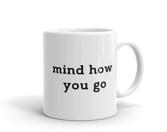Pode incluir: Caneca de café de cerâmica branca com texto preto que diz "mind how you go"