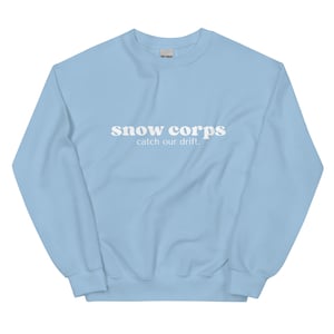 May include: A light blue sweatshirt with the text "snow corps catch our drift." printed in white.