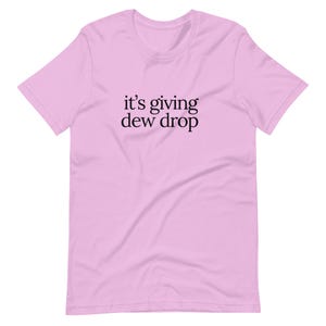 May include: A light pink t-shirt with the phrase "it's giving dew drop" printed in black. The shirt has short sleeves and a crew neck.