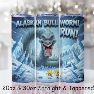 Puede incluir: Un vaso azul con una ilustración de dibujos animados de un gusano grande con la boca abierta y las palabras "ALASKAN BULL WORM! RUN!". El diseño incluye formaciones de hielo y dos personajes de dibujos animados huyendo. El vaso está disponible en tamaños de 591ml y 887ml.