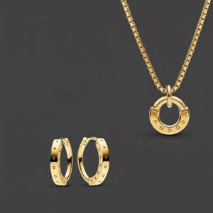 Könnte beinhalten: Ein goldfarbenes Schmuckset mit einer Halskette und einem Paar Creolen. Die Halskette hat eine Kette und einen kreisförmigen Anhänger mit dem eingravierten Wort "Pandora". Die Ohrringe sind kleine Reifen mit demselben eingravierten Wort.
