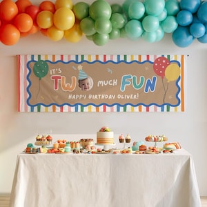 May include: A rectangular birthday banner with a tan center and striped border, featuring the text 'IT'S TWO MUCH FUN' and 'HAPPY BIRTHDAY OLIVER' with a photo of a child in a party hat, displayed above a table with a cake and various desserts.