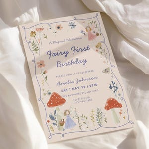 May include: A light beige invitation card with a whimsical fairy theme. The text reads "Fairy First Birthday" with floral and mushroom illustrations. The card includes event details and RSVP information.
