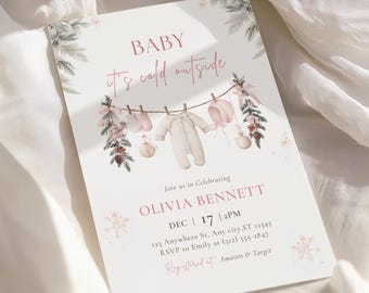 Peut inclure: Une carte d'invitation rectangulaire pour une fête prénatale avec le texte BABY it's cold outside, illustrée de vêtements de bébé, de branches de pin et de pommes de pin sur une corde. La carte indique les détails pour Olivia Bennett le 17 déc.