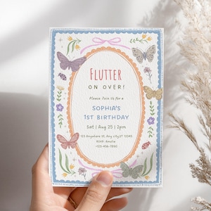 May include: A rectangular birthday invitation card featuring a central oval frame with a scalloped orange border. The text reads: Flutter on over! Please join us for a Sophia's 1st birthday, Sat Aug 25 2pm, 123 Anywhere St, Any city, ST 12345, RSVP: Amelia +123-456-7890.