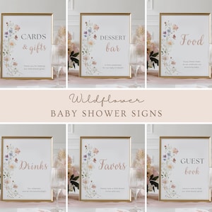 May include: A collection of framed baby shower signs with gold frames and floral accents. The signs include text such as "Cards & Gifts", "Dessert Bar", "Food", "Drinks", "Favors", and "Guest Book". The signs are decorated with watercolor wildflowers.
