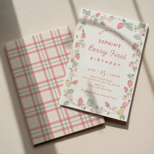 Puede incluir: Una invitación de cumpleaños con el texto "SOPHIA'S Berry First BIRTHDAY" rodeada por un borde de fresas y hojas. La invitación incluye la fecha, la hora y el lugar. Un cuaderno a juego con un patrón de cuadros rosas y verdes está al lado de la invitación.