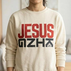 May include: Cream-colored sweatshirt with the words "JESUS IS KING" in red and black block letters. The sweatshirt has a crew neck and ribbed cuffs and hem. The text is embroidered on the front.