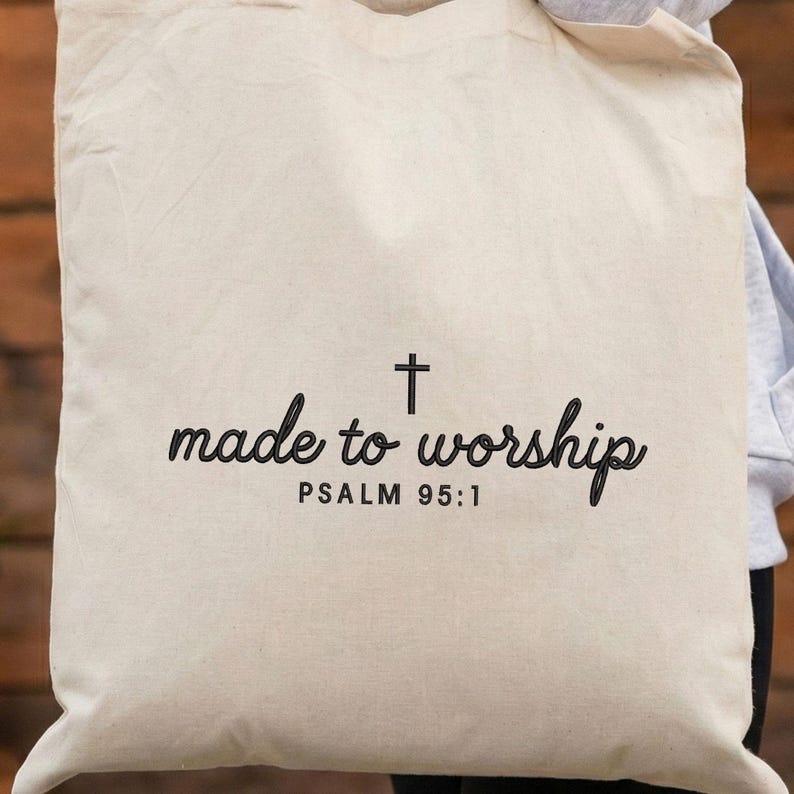 May include: Cream-colored tote bag with the words "made to worship" and a cross symbol printed in black. The text "PSALM 95:1" is printed below the main text. The bag is made of a sturdy fabric.