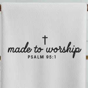 May include: White towel with the words "made to worship" in a script font, a cross, and the text "PSALM 95:1" in a simple font. The towel is hanging on a wooden rod.
