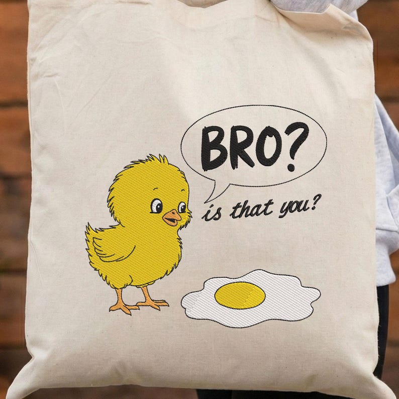 May include: Cream-colored tote bag featuring an embroidered yellow chick and a fried egg. A speech bubble reads "BRO? is that you?" in black text. The design is whimsical and playful, suitable for carrying groceries or personal items.