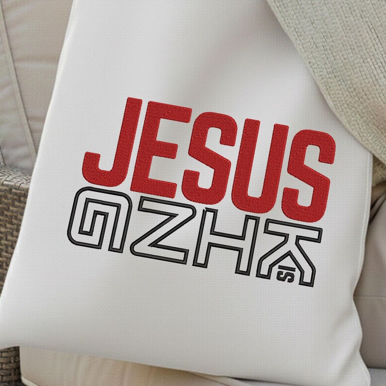 May include: White square pillow with the word "JESUS" in red, embroidered in a bold, sans-serif font. Below, the letters "GZHK" are embroidered in black, outlined with a double line. The pillow is on a neutral-toned surface.
