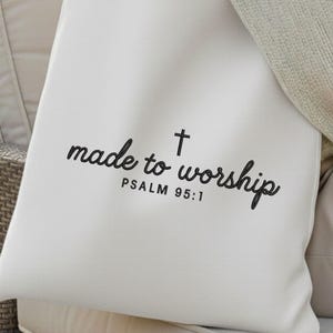 May include: Cream-colored pillow with the words "made to worship" and a cross symbol printed in black script. The text "PSALM 95:1" is printed below the main text. The pillow is on a neutral-toned surface.