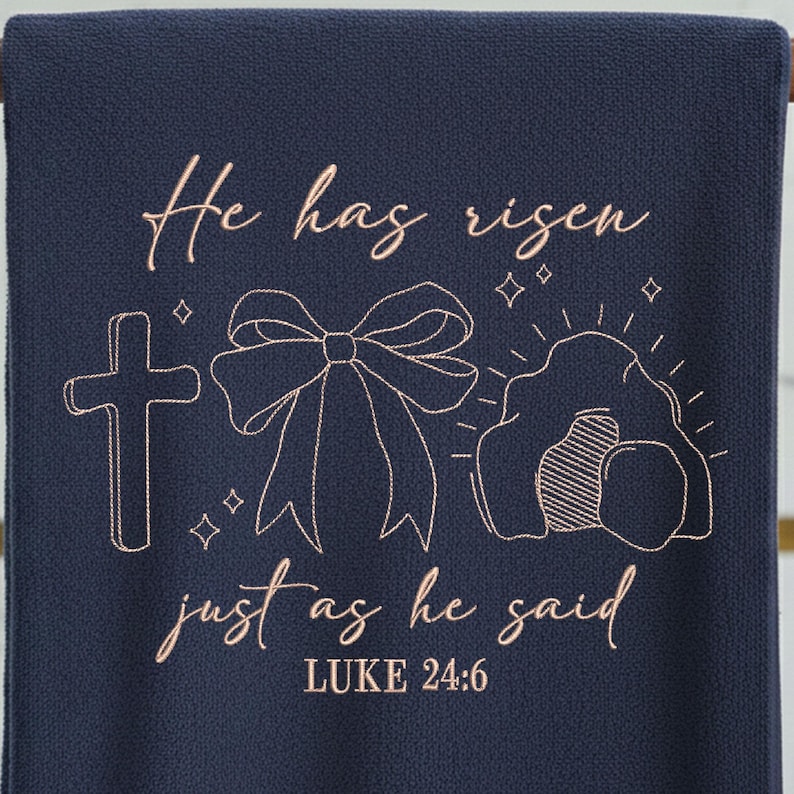 May include: Navy blue decorative towel with embroidered text and imagery. The text reads "He has risen, just as he said, Luke 24:6." The design includes a cross, a bow, and an empty tomb, all in a light brown color.