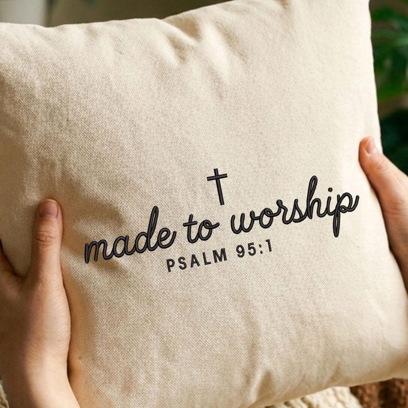 May include: A square, beige pillow with the words "made to worship" in a black script font, along with a cross and the text "PSALM 95:1". The pillow is held by hands.
