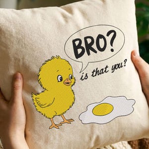 May include: Cream-colored square pillow with an embroidered cartoon chick and fried egg design. The chick is yellow with black outlines, and the egg has a yellow yolk. Text in a speech bubble reads "BRO? is that you?"