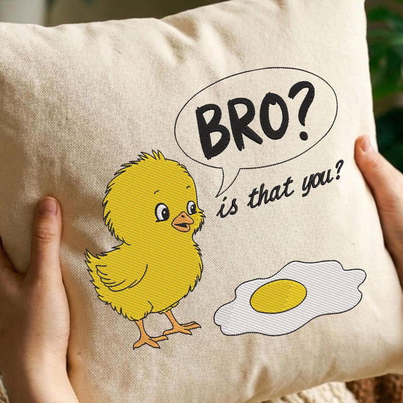 May include: Cream-colored square pillow with an embroidered cartoon chick and fried egg design. The chick is yellow with black outlines, and the egg has a yellow yolk. Text in a speech bubble reads "BRO? is that you?"