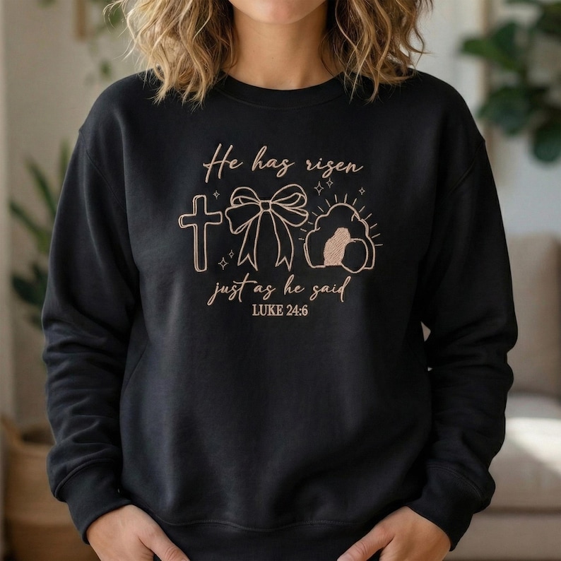 May include: Black sweatshirt with the text "He has risen just as he said" and a graphic of a cross, bow, and tomb. The text and graphics are in a light brown color.