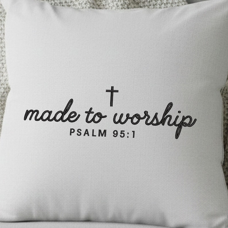 May include: A square, light gray pillow with the words "made to worship" in a black script font, a black cross, and the text "PSALM 95:1" in a smaller font. The pillow is made of a textured fabric.
