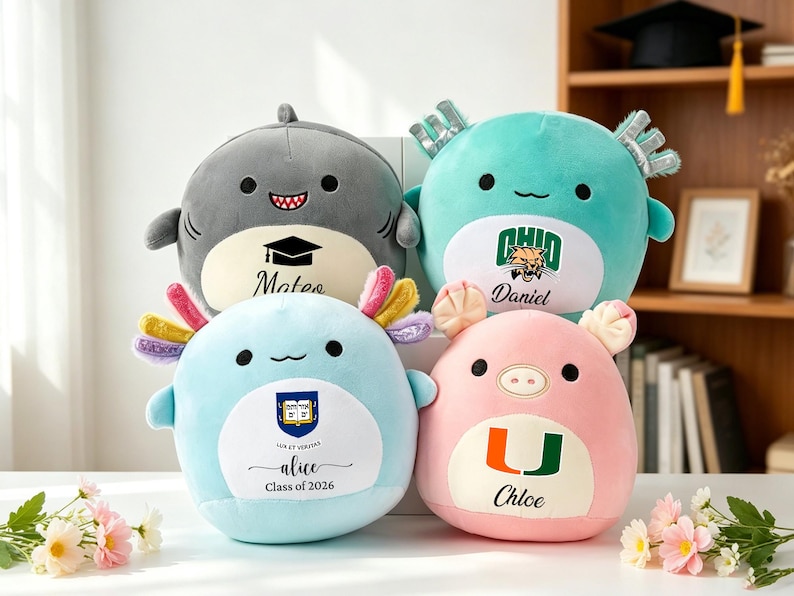 May include: Four plush toys in the shape of a shark, axolotls, and a pig. The shark is gray, the axolotls are blue and teal, and the pig is pink. Each has a name and a logo or graduation cap printed on it.