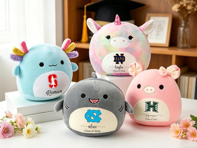 May include: Four plush toys: a blue axolotl, a unicorn, a shark, and a pink pig. Each has a school logo and a name with "Class of 2026". The axolotl has a Stanford logo and the name "Roman". The unicorn has a Notre Dame logo and the name "Layla". The shark has a UNC logo and the name "Alice". The pig has a Hawaii logo and the name "Harper".