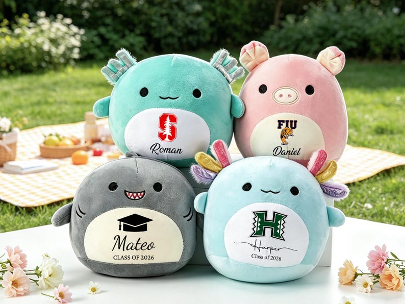May include: Four plush toys in the shape of animals, including a shark, axolotl, and pig. Each has a personalized design with a name, school logo, and graduation year. The toys are in shades of blue, gray, and pink.