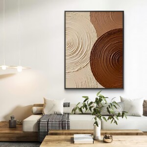 May include: Abstract wall art featuring a textured design of overlapping circles in shades of beige and brown. The artwork is framed in black and hangs on a white wall. The piece adds a modern touch to any living space.