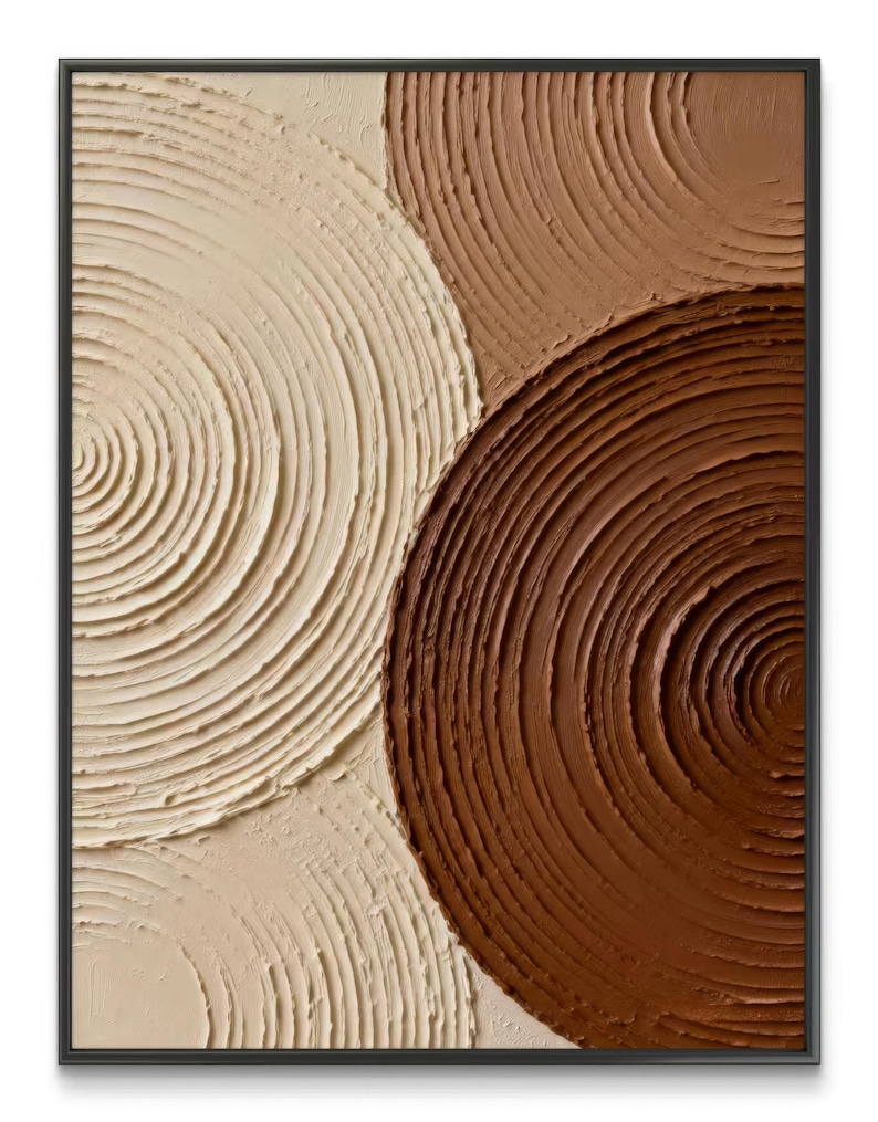May include: Abstract wall art in a black frame. The artwork features a textured surface with three overlapping circular shapes in shades of cream, tan, and brown. The circles have a spiral pattern, creating a sense of depth and movement. The piece is a modern, minimalist design.
