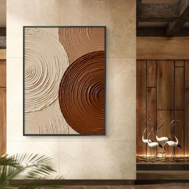 May include: Abstract wall art featuring a black framed canvas with a textured design. The artwork showcases three overlapping circular shapes in shades of beige, tan, and brown. The textured surface creates a sense of depth and visual interest.
