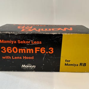 May include: A rectangular black and yellow cardboard box for a Mamiya Sekor Lens 360mm F6.3 with Lens Hood for Mamiya RB. The box features orange text reading Mamiya Sekor Lens 360mm F6.3 with Lens Hood and the Mamiya Camera Co. Ltd. logo.