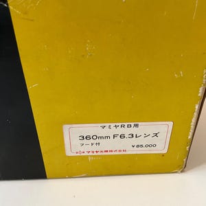 May include: A yellow and black box featuring a white rectangular label with Japanese text that reads Mamiya RB, 360mm F6.3 lens, and includes a hood. The label also displays the manufacturer name Mamiya Optical Co., Ltd. in Japanese characters.