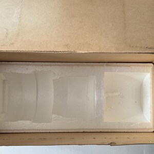 May include: A rectangular cardboard shipping box with an open top, containing a white molded polystyrene foam insert. The insert features custom-shaped recessed compartments designed to hold and protect items during transport and storage.