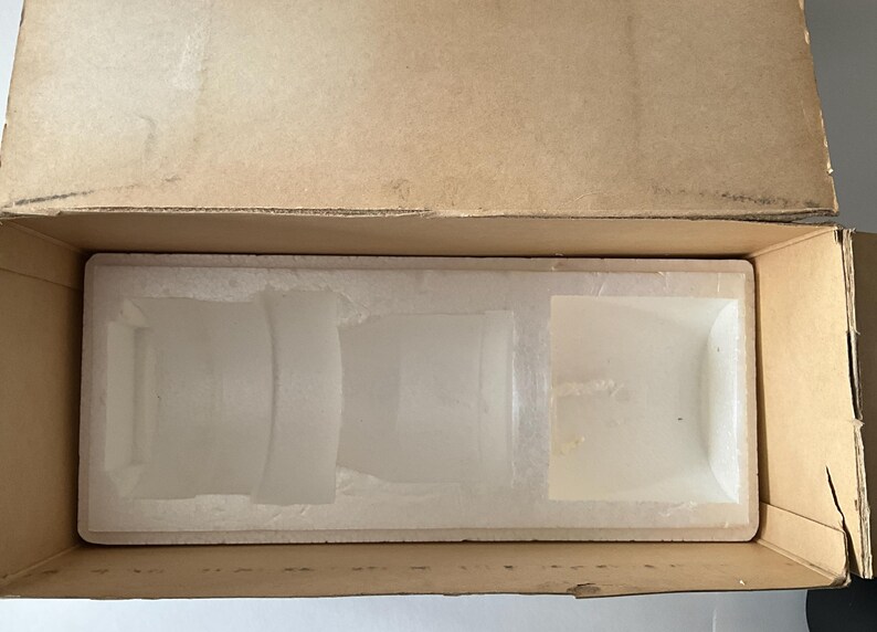 May include: A rectangular cardboard shipping box with an open top, containing a white molded polystyrene foam insert. The insert features custom-shaped recessed compartments designed to hold and protect items during transport and storage.