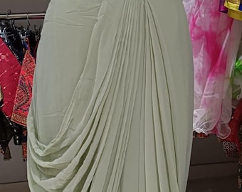 May include: A light green, draped saree-style dress on a mannequin. The top is a textured, light green fabric, and the skirt features flowing, pleated fabric. The dress is displayed in a clothing store.